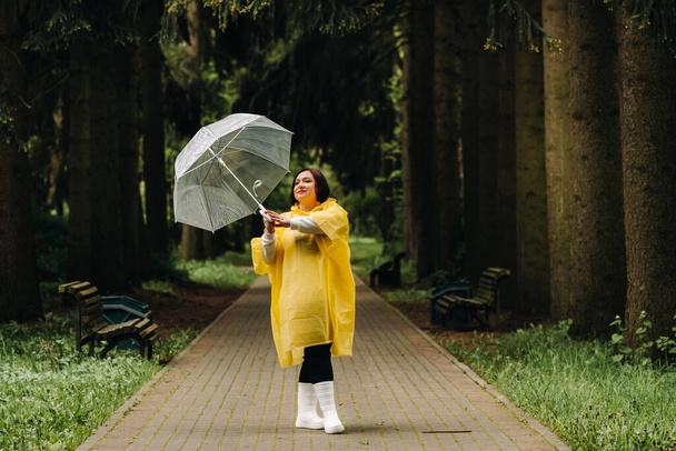 a woman in a yellow raincoat and an umbrella walks in the park and garden in summer. - Фото, изображение