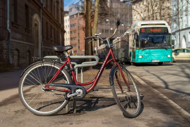 Red bicycle Helkama parked on the city street in Tallinn city center (Estonian - Kesklinn). Public city bus on background. Warm sunny spring day.  - Foto, afbeelding