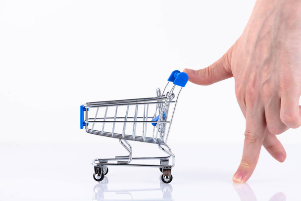 Female hand with fingers in the form of a walking man, pushing a shopping cart, isolated on a white background. Copy space. - Photo, image