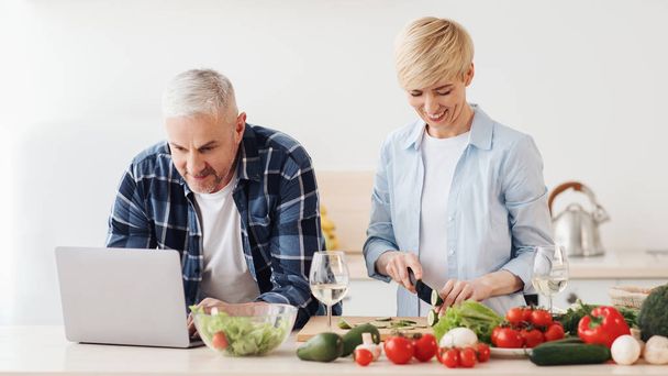 Szczęśliwy w średnim wieku 50s para za pomocą laptopa, przygotowanie zdrowej żywności - Zdjęcie, obraz