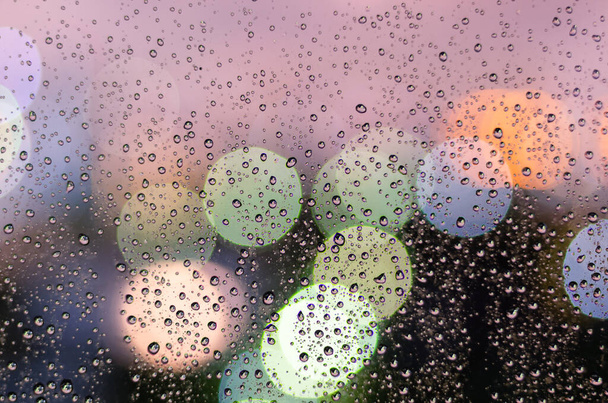 Πτώση βροχής σε γυάλινο παράθυρο την εποχή των μουσώνων με πολύχρωμο φως bokeh από τα κτίρια της πόλης φόντο. - Φωτογραφία, εικόνα