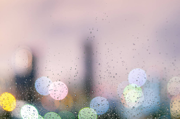 Regen druppel op glas venster in moesson seizoen met kleurrijke bokeh licht van de stad gebouwen achtergrond. - Foto, afbeelding