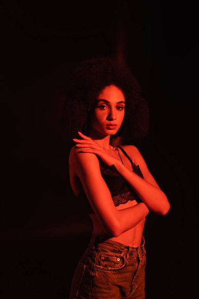 African american woman in bra looking at camera in red light isolated on black  - 写真・画像