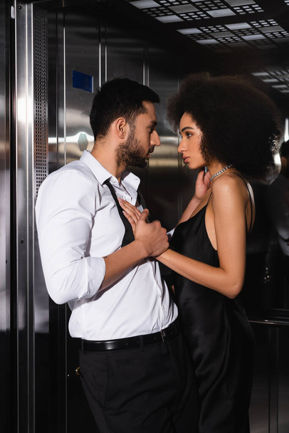 Side view of bearded man touching african american girlfriend in elevator  - Photo, Image