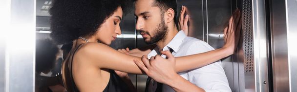 Boční pohled na muže v košili dotýkající se africké americké přítelkyně ve výtahu, banner  - Fotografie, Obrázek