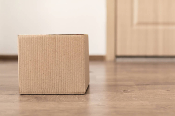 Доставленная картонная коробка лежит на полу рядом с дверью квартиры - Фото, изображение