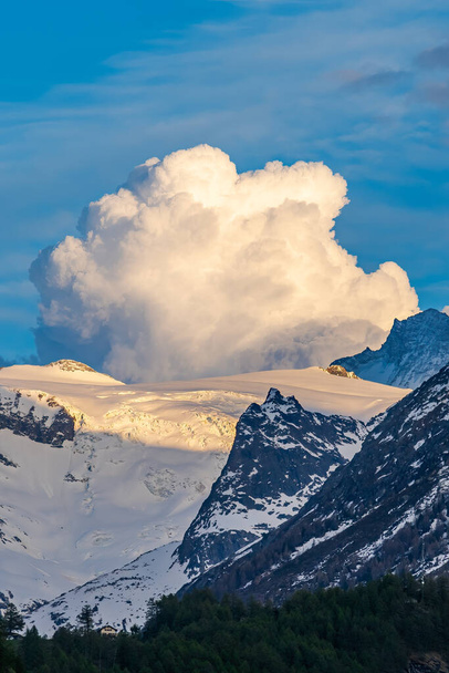 Горный ландшафт над Валь-Херансом в Швейцарии на закате с персиками, покрытыми снегом и очень большим облаком - Фото, изображение