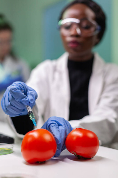 Close-up van chemicus wetenschapper die organische tomaat injecteert met pesticiden - Foto, afbeelding