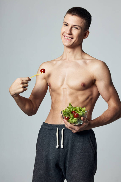 Веселий спортивний чоловік з м'язистим голим тілом їсть овочевий салат
 - Фото, зображення