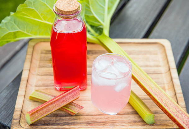 自家製ルバーブシロップ(ルバーブ) 。ボトルとガラスの素敵なピンクの液体シロップとジュースと氷のキューブは、ルバーブの茎で飾られたトレイ上のガラスを飲んでいます。春の飲み物をリフレッシュ. - 写真・画像