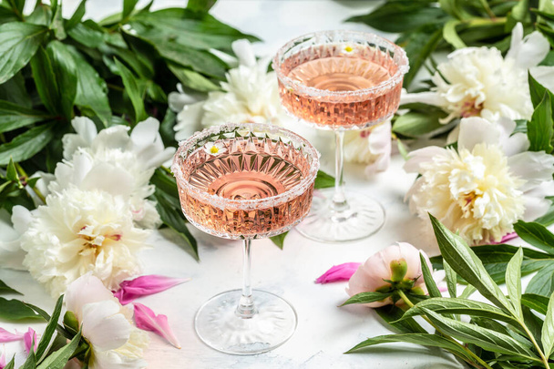 Delicious rose wine in glasses and many peony flowers. Summer celebration, wedding greeting card, invitation concept - Photo, Image