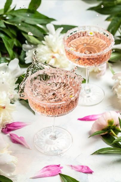 Delicious rose wine in glasses and many peony flowers. Summer celebration, wedding greeting card, invitation concept - Photo, Image