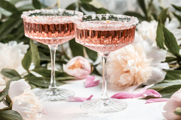 Růžové víno ve skleněných a pivoňkových květinách na bílém pozadí, Letní oslava, svatební přání, koncept pozvání. - Fotografie, Obrázek