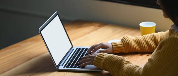 Una mujer está escribiendo en una computadora portátil de pantalla blanca en blanco que poner en un escritorio de madera. - Foto, imagen