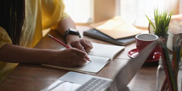 Przycięty obraz kobiety piszącej na notebooku, który umieszcza na biurku i otoczony komputerowym laptopem i notebookiem na wygodnym salonie jako tło. - Zdjęcie, obraz