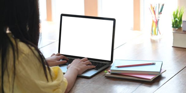 Nahaufnahme stilvolle Frau tippt auf Computer-Laptop mit weißem leeren Bildschirm, während sie am hölzernen Schreibtisch über gemütlichem Wohnzimmer als Hintergrund sitzt. - Foto, Bild