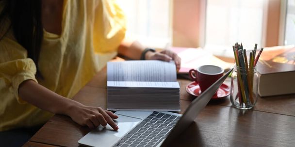 Nahaufnahme Frau entspannt und mit einem Computer-Laptop, während sie am hölzernen Schreibtisch über gemütlichen Wohnzimmerfenstern als Hintergrund sitzt. Nachhilfe und Online-Lernkonzept. - Foto, Bild