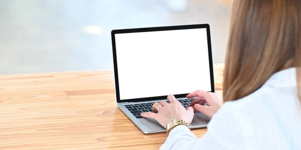 Gesneden beeld van een mooie vrouw met behulp van een computer laptop met wit leeg scherm terwijl zitten aan de witte werktafel over comfortabele woonkamer als achtergrond. - Foto, afbeelding