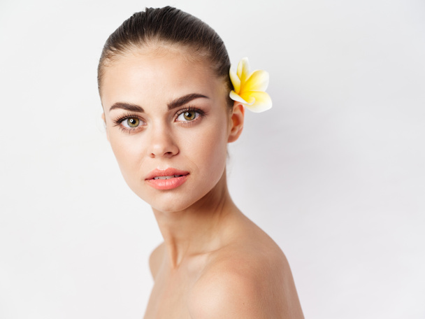 woman with bare shoulders with yellow flower on  light background. High quality photo - Foto, Bild