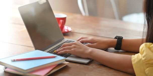 Przycięte strzał kobieta, która wygląda dobrze w żółtej bawełnianej koszuli patrząc i pisząc na laptopie komputera siedząc przy drewnianym biurku nad wygodnym salonie jako tło. - Zdjęcie, obraz