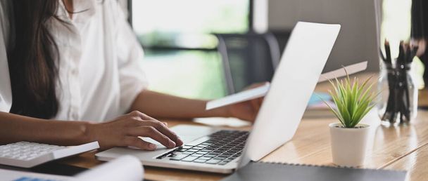 L'immagine ritagliata della mano di una donna sta lavorando con un computer portatile alla scrivania di legno. - Foto, immagini