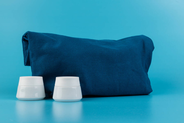 Βάζο για καλλυντική κρέμα χεριών, ποδιών ή προσώπου κοντά σε μπλε υφασμάτινη τσάντα. Καθαρισμός, φροντίδα. Αντιγραφή χώρου - Φωτογραφία, εικόνα