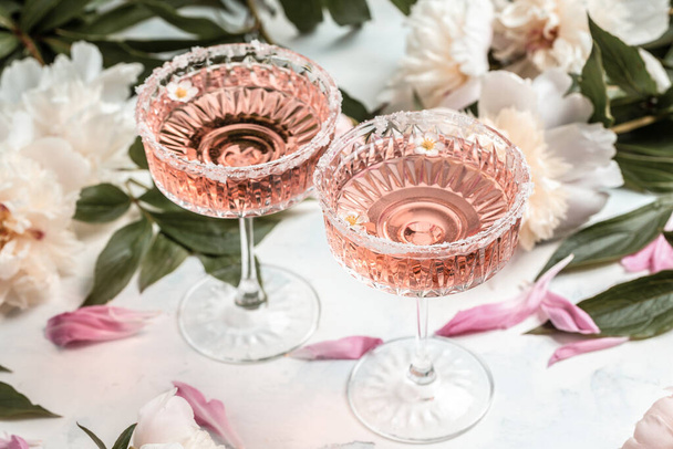 Νόστιμο ροζέ κρασί σε ποτήρια και πολλά παιώνια λουλούδια. Καλοκαιρινή γιορτή, γαμήλια ευχετήρια κάρτα, πρόσκληση - Φωτογραφία, εικόνα