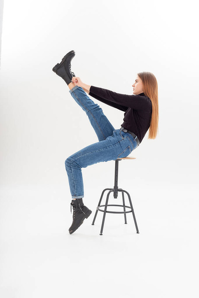 young attractive caucasian woman in black turtleneck, blue jeans pulls boots on - Photo, Image