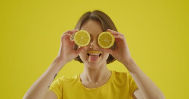 Sarı arka planda dilimlenmiş limonu olan şık genç bir kadın. - Video, Çekim