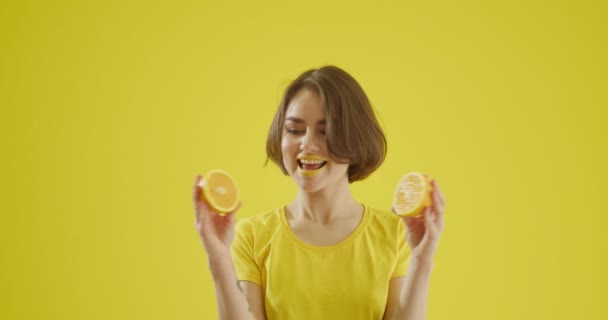 Stijlvolle jonge vrouw met gesneden citroen op gele achtergrond - Video