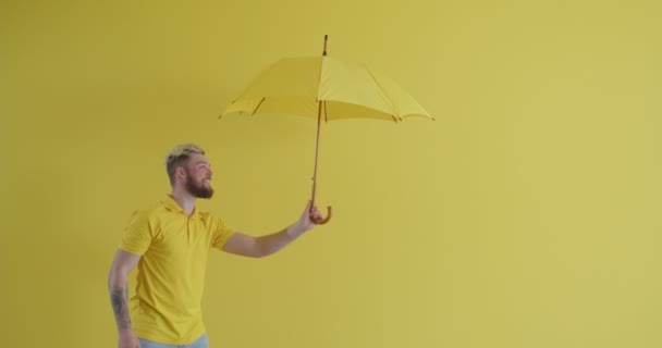 Young man holding yellow umbrella in stormy weather against color background - Footage, Video