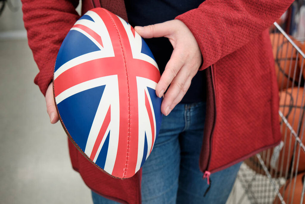 Жінка в магазині купує регбі і американський футбольний м'яч з друком британського прапора. - Фото, зображення