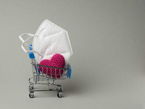 Medizinische Einmalmaske in einem Miniaturwagen auf grauem Hintergrund. Verkauf von Medizinprodukten online - Foto, Bild