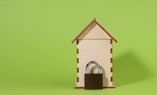 miniature wooden house and metal lock on a green background, security concept. Private property - Photo, Image