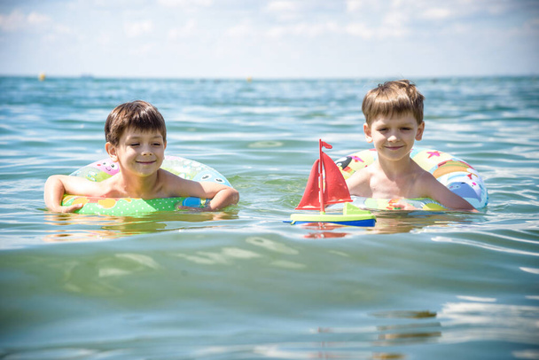 幸せな子供たちはビーチで海サーフィンを楽しんでいます。壊れた波の上でインフレータブルリングに乗る上で楽しいカップルの子供たち。家族の夏のキャンプでの旅行生活、水泳活動。熱帯の島の休暇. - 写真・画像