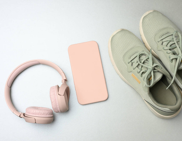 roze sneakers, draadloze koptelefoon, een smartphone op een grijze achtergrond. Dingen en gadgets voor sport, hardlopen, platte lay - Foto, afbeelding