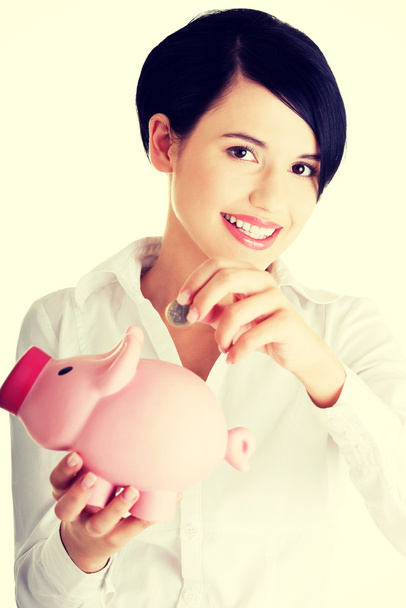 Businesswoman putting a coin into a piggy bank - Foto, afbeelding