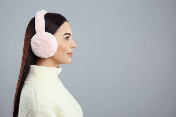 Beautiful young woman wearing earmuffs on light grey background. Space for text - Foto, immagini