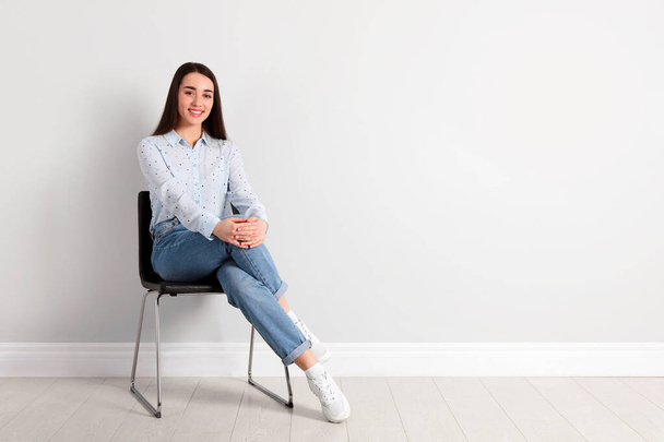 Jovem mulher sentada na cadeira perto da parede branca no escritório, espaço para texto - Foto, Imagem