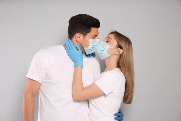 Couple in medical masks and gloves trying to kiss on light background - Fotografie, Obrázek