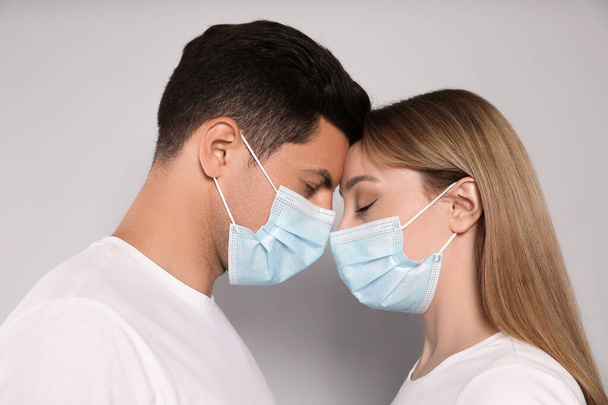 Couple in medical masks trying to kiss on light background - Fotó, kép