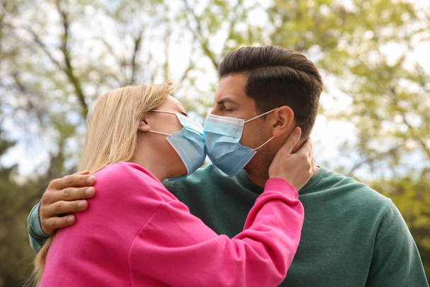 Couple dans des masques médicaux essayant de baiser à l'extérieur - Photo, image
