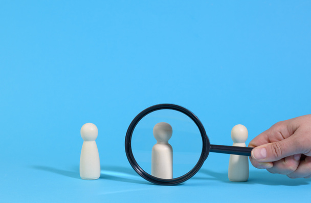 wooden figures of men stand on a blue background and a black magnifying glass. Recruitment concept, search for talented and capable employees, career growth - Photo, Image