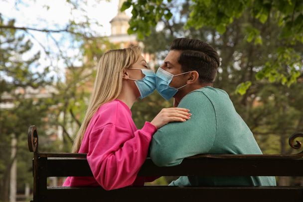 Couple in medical masks trying to kiss outdoors - Photo, Image