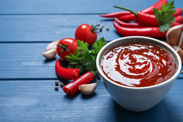 Spicy chili sauce in bowl on blue wooden table, space for text - Foto, imagen