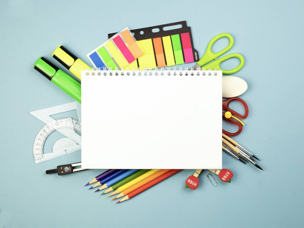 Stationery school supplies on blue background with sketchbook centered, stationery around the album. Flat lay. Back to school. School learning concept. Copy space. - Foto, Bild