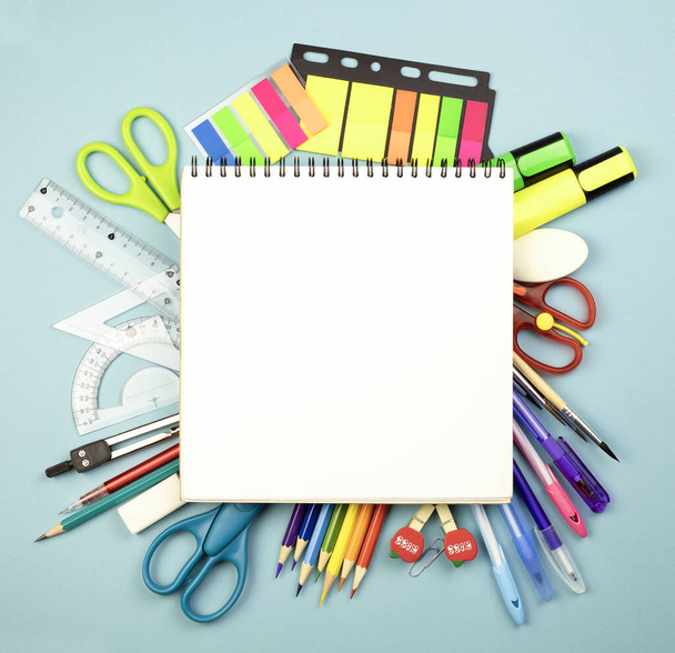 Stationery school supplies on a blue bright background with a white notepad in the center, colored markers and pencils, rulers, scissors, pens. Back to school. School learning concept. Copy space. - Foto, imagen