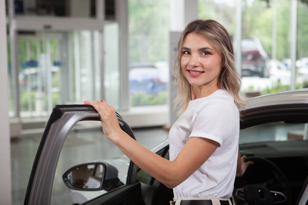 Beautiful young woman smiling to the camera while getting inside a new automobile - Foto, Imagen