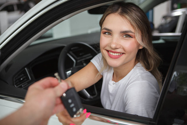 Beautiful happy woman sitting in her new automobile, receiving car keys from salesman - Photo, Image