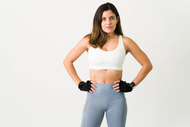 Portrait d'une jeune femme en bonne santé posant avec des vêtements de sport et des gants avant de faire de l'exercice avec des poids au gymnase - Photo, image